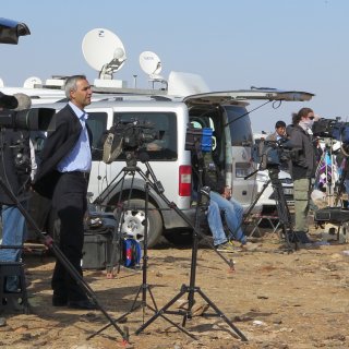 Reporters outside of a car looking away with camera equipment around